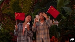 FILE - Chinese women hold up the Chinese national flags as they take photos near a floral display marking China's 75th National Day in Beijing, Oct. 2, 2024.