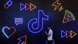 2019年10月18日，在浙江杭州举行的国际智能产品博览会上，一名男子拿着手机走过中国公司字节跳动应用程序抖音的标志。（资料照片）