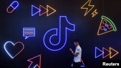 2019年10月18日，在浙江杭州舉行的國際智能產品博覽會上，一名男子拿著手機走過中國公司字節跳動應用程序抖音的標誌。（資料照片）