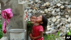 Seorang anak perempuan menggendong seorang bayi, minum air dari pancuran air di desa Balua yang hancur akibat gempa bumi, di distrik Gorkha, Nepal, 30 April 2015 (AP Photo/Wally Santana)