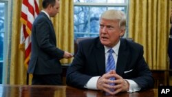 President Donald Trump sits at his desk as he waits for White House Chief of Staff Reince Priebus, left, to deliver three executive orders for his signature, Jan. 23, 2017, in the Oval Office of the White House in Washington.