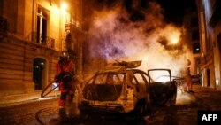 Un sapeur-pompier essaie d'éteindre le feu sur une voiture incendiée sur les Champs-Elysées après la défaite du PSG, France, le 23 août 2020. 