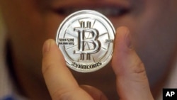 FILE - A man holds a token bearing the symbol of a cryptocurrency at his shop in Sandy, Utah. The tiny Marshall Islands is creating its own digital cryptocurrency in order to raise hard cash to pay bills and boost the economy.