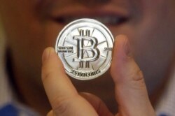 FILE - A man holds a token featuring the symbol of a cryptocurrency at his shop in Sandy, Utah.