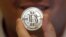  FILE - A man holds a token bearing the symbol of a cryptocurrency at his shop in Sandy, Utah. 