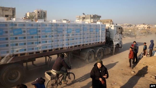 People watch as a truck loaded with humanitarian aid drives through a devastated street in Khan Younis in the southern Gaza Strip on Jan. 30, 2025.