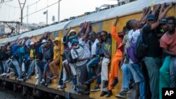 Train commuters hold on to the side of an overcrowded passenger train in Soweto, South Africa, Monday, March 16, 2020. 