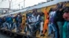 Train commuters hold on to the side of an overcrowded passenger train in Soweto, South Africa.