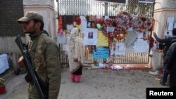 FILE - A soldier stands near a woman reading messages left by people for the victims of the Taliban attack on a school, in Peshawar, Pakistan, Dec. 23, 2014. 