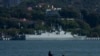 FILE - A man sits on a boat fishing near a Chinese guided missile destroyer Shangqiu docked in Xiamen in southeast China's Fujian province, Dec. 26, 2023.