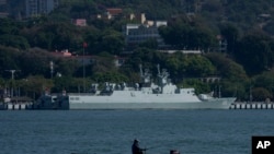 FILE - A man sits on a boat fishing near a Chinese guided missile destroyer Shangqiu docked in Xiamen in southeast China's Fujian province, Dec. 26, 2023.