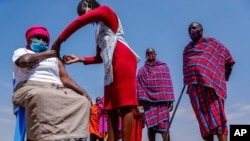 Maasai men line up to receive the AstraZeneca coronavirus vaccine as a woman receives a jab at a clinic in Kimana, southern Kenya, Aug. 28, 2021. 