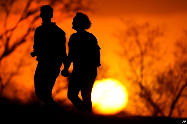 FILE  In this March 10, 2021 file photo, a couple walks through a park at sunset in Kansas City, Mo.. (AP Photo/Charlie Riedel, File)