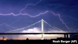 FILE - In this Aug. 16, 2020, file photo, lightning forks over the San Francisco-Oakland Bay Bridge as a storm passes over Oakland, Calif. Numerous lightning strikes led to brush fires throughout the area. 