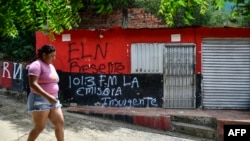 Una mujer pasa frente a una casa con un grafiti del grupo guerrillero ELN, en el municipio de El Zulia, cerca de Cúcuta, Colombia, el 4 de julio de 2023. (Foto por Schneyder MENDOZA / AFP)