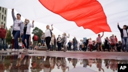 Belarusian opposition supporters carry a huge old Belarusian national flag as rally toward Independence Square in Minsk, Belarus, Aug. 23, 2020. 
