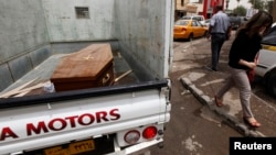 A woman walks past a truck carrying a wooden coffin of a man killed during an attack on liquor stores in Baghdad, Iraq, May 15, 2013. 