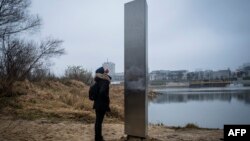 Seorang perempuan memperhatikan pilar metal yang tiba-tiba terpasang di pinggiran Sungai Vistula, di Warsawa, Ibu Kota Polandia, 10 Desember 2020. Belum ada pihak yang mengaku memasang pilar itu. (Foto: AFP)
