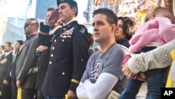Former U.S. Air Force Senior Airman Brian Kolfage, center, a double amputee from the Iraq war, sits in a wheelchair next to his wife Ashley, right, who holds their daughter Paris, during a "Salute to Service" tribute honoring U.S. veterans, Nov. 10, 2014, in New York.