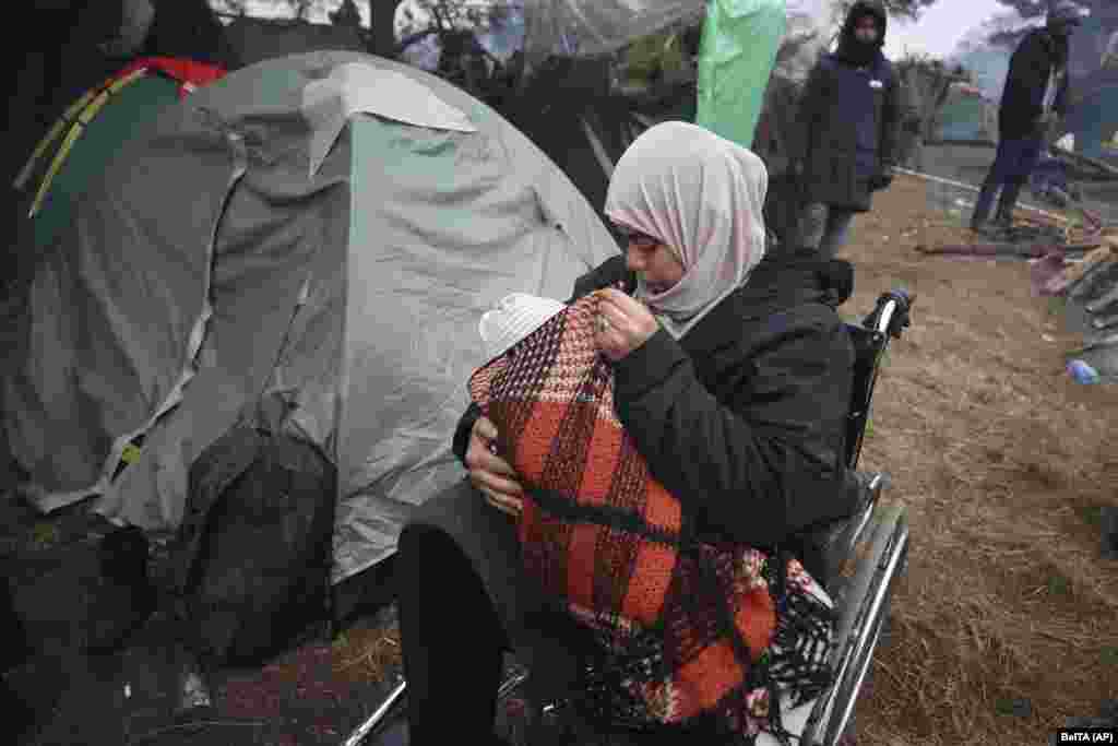 Seorang perempuan menggendong anaknya sambil duduk di kursi roda ketika ratusan migran, sebagian besar dari Timur Tengah, berkumpul di perbatasan Belarus-Polandia dekat Grodno, Belarus, Jumat, 12 November 2021. (Foto: AP)