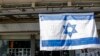 Sebuah bendera Israel berkibar di luar sebuah gedung di Kota Kiryat Shmona, Israel utara, dekat perbatasan Lebanon pada 11 Februari 2024. (Foto: AFP)