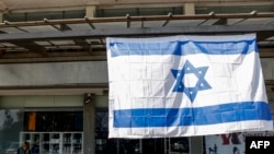 Sebuah bendera Israel berkibar di luar sebuah gedung di Kota Kiryat Shmona, Israel utara, dekat perbatasan Lebanon pada 11 Februari 2024. (Foto: AFP)