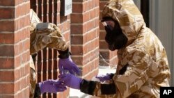 Specialist team members in military protective suits use a jar in the front doorway as they search the fenced-off John Baker House for homeless people on Rollestone Street in Salisbury, England, July 6, 2018. British police are scouring sections of Salisbury and Amesbury in southwest England, searching for a container feared to be contaminated with traces of the deadly nerve agent Novichok.