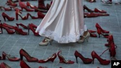 An actress walks near a line of red shoes representing murdered women, as part of a performance during the International Women's Day strike "A Day Without Women" in Mexico City, Monday, March 9, 2020.