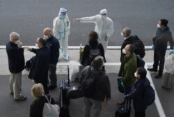 A worker in protective coverings directs members of the World Health Organization (WHO) team on their arrival at the airport in Wuhan in central China's Hubei province, Jan. 14, 2021.