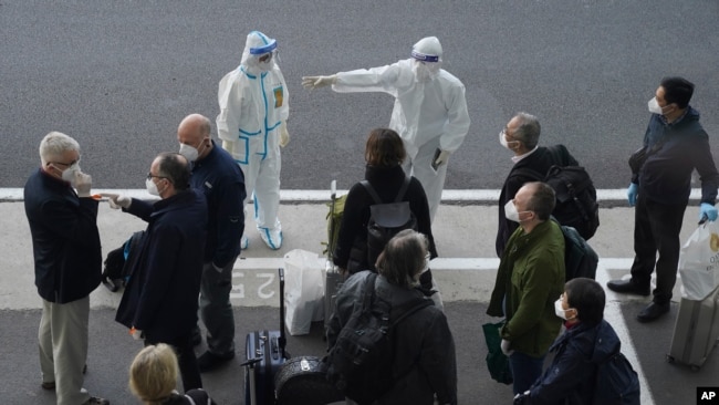 A worker in protective coverings directs members of the World Health Organization (WHO) team on their arrival at the airport in Wuhan in central China's Hubei province on Thursday, Jan. 14, 2021. A global team of researchers arrived Thursday in the…