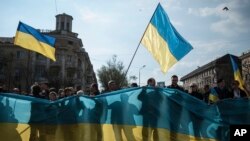 Para pendukung pemerintah Ukraina berpawai sambil memegang bendera Ukraina raksasa di Mariupol, Ukraina selatan (23/4).