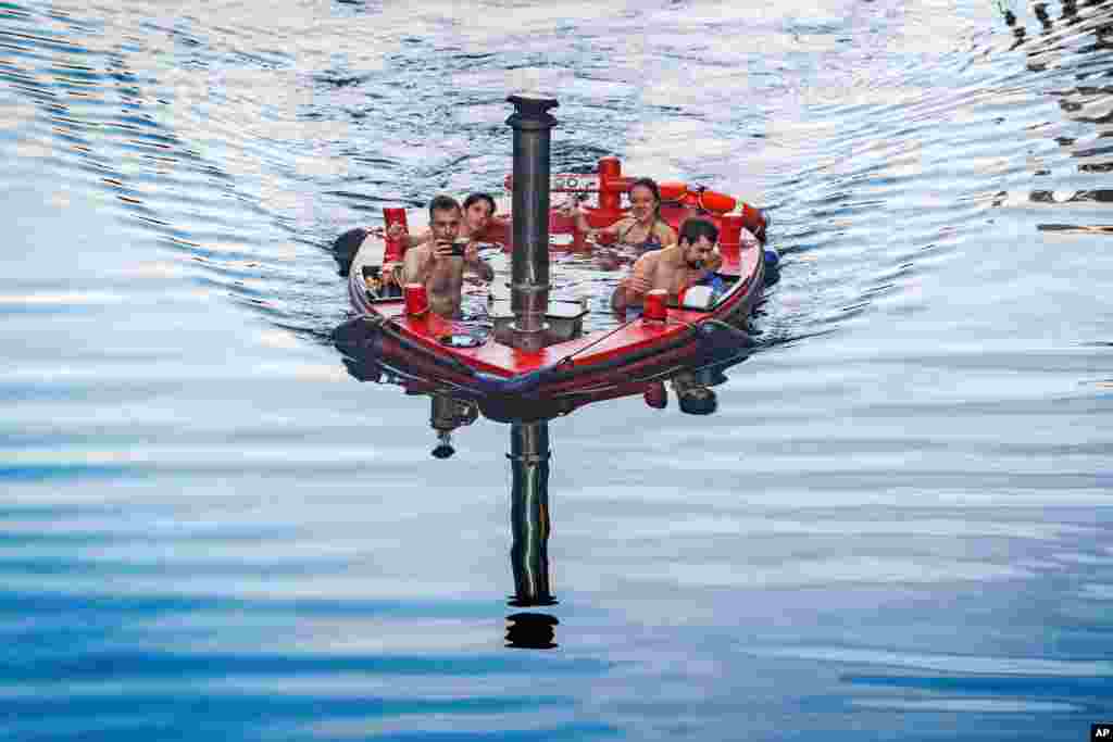 A group of people sit inside a hot tub boat sailing on the River Thames at Canary Wharf in London.