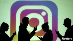 FILE PHOTO: Silhouettes of mobile users are seen next to a screen projection of Instagram logo in this picture illustration