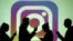 FILE PHOTO: Silhouettes of mobile users are seen next to a screen projection of Instagram logo in this picture illustration