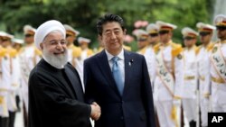 Japanese Prime Minister Shinzo Abe, center, shakes hands for the cameras with Iranian President Hassan Rouhani, during the official arrival ceremony, at the Saadabad Palace in Tehran, Iran, June 12, 2019. 