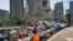 FILE - A homeless man sits at his street-side tent along Interstate 110 along downtown Los Angeles' skyline, May 10, 2018. Thousands of homeless people sleep on the streets of Los Angeles County. Southern California Public Radio station KPCC reports probl