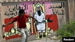 A protester throws a chain next to a graffiti on the wall depicting the newly appointed governor of Luxor Adel Mohamed al-Khayat, as a terrorist, as protests gather in front of the governorate building to protest his appointment in Luxor, June 19, 2013. 