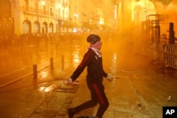 An anti-government protester prepares to throw stones at the riot police, during a protest against the new government, near the parliament square, in Beirut, Lebanon, Jan. 22, 2020.