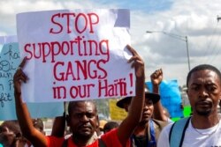 FILE - A protester holds a sign with a message to stop supporting gangs during a protest in Port-au-Prince, Haiti, Dec. 10, 2020.