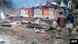 Local residents stand beside a burning house following cross-border shelling between Pakistani and Indian forces in Tehjain village at the Line of Control in Neelum Valley, Pakistan-administered Kashmir, Nov. 13, 2020.