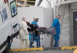FILE - A patient with symptoms related to COVID-19 is brought to a field hospital by workers in full protective gear in Leblon, Rio de Janeiro, Brazil, June 4, 2020.