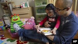 Christopher Astacio membaca dengan putrinya Cristina, 2, yang didiagnosis memiliki bentuk autisme yang lebih ringan, di rumah mereka di New York. (Foto: Dok)