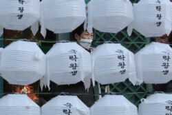 A woman wearing a face mask stands behind lanterns decorated for upcoming celebration of Buddha's birthday on April 30, at Jogye temple in Seoul, South Korea, Tuesday, Feb. 18, 2020.