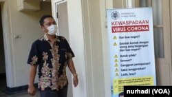 Seorang staf UGM melintas di depan poster terkait Virus Corona di kampus tersebut. (Foto:VOA/ Nurhadi)