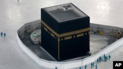 ພວກຄົນງານຊີດຢາຂ້າພະຍາດໃສ່ພື້ນອ້ອມຫີນສັກສິດ ຊົງສີ່ຫຼ່ຽມ ທີ່ເອີ້ນວ່າ Kaaba, ຕັ້ງຢູ່ທີ່ວັດໃຫຍ່ ໃນເມືອງສັກສິດ ເມັກກາ ຂອງປະເທດຊາອຸດີອາຣາເບຍ, ວັນທີ 7 ມີນາ 2020.