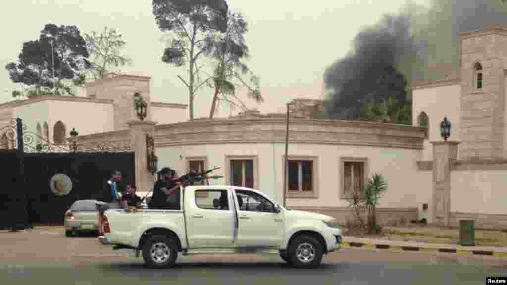 Armed men aim their weapons from a vehicle as smoke rises in the background near the Libyan parliament building in Tripoli May 18, 2014.