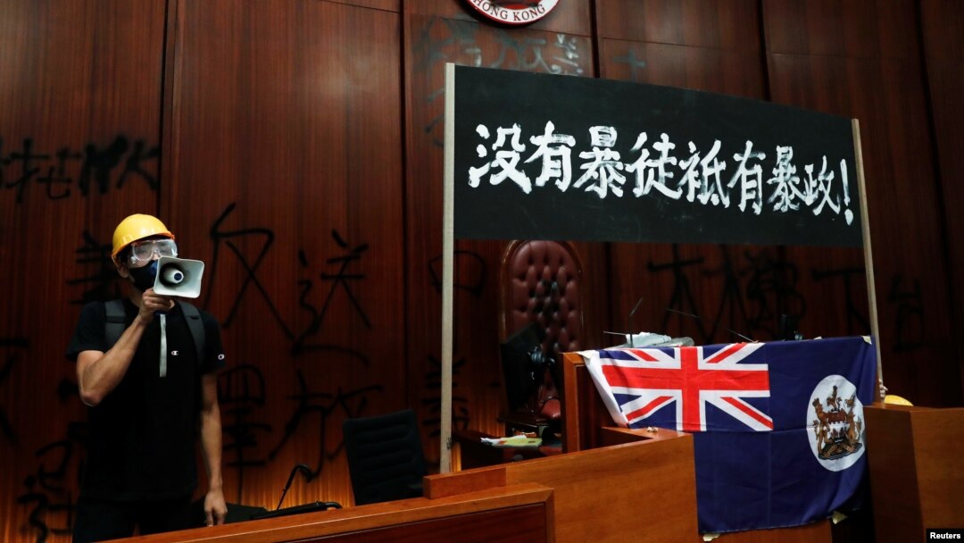 一名进入香港立法会的抗议者站在挂在立法会内的港英旗帜旁使用扩音喇叭讲话。（2019年7月1日）
