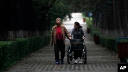 FILE - An elderly Chinese woman accompanied by her caregiver walks down a tree lined lane in Changchun in northeastern China's Jilin province, Aug. 27, 2010.