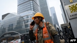 A worker uses a cell phone outside a construction site in Beijing on October 31, 2024. 