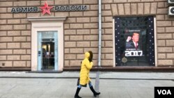 Seorang perempuan melewati toko pakaian tentara Rusia di seberang Kedutaan AS di Moskow, yang memasang poster Donald Trump pada hari pelantikannya menjadi Presiden ke-45 AS, 20 Januari 2016. (D. Schearf/VOA) 